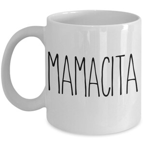 May include: White ceramic mug with the word "MAMACITA" printed in black, handwritten-style letters. The mug has a curved handle and a simple, clean design. A perfect gift for Mother's Day or any special occasion.