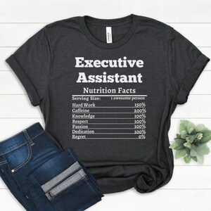 May include: A dark gray t-shirt with white text that reads "Executive Assistant Nutrition Facts" and lists the percentage of hard work, caffeine, knowledge, respect, passion, dedication, and regret needed for the job.
