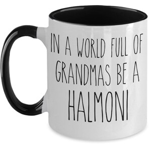 May include: White ceramic coffee mug with a black handle and black rim. The mug has black text that reads "In a world full of grandmas be a halmoni".