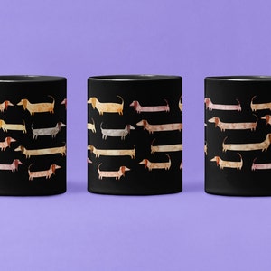 May include: Three black coffee mugs with a repeating pattern of watercolor dachshunds in various colors. The dogs are in shades of tan, pink, and gray, set against a solid black background. The mugs have a standard handle design.