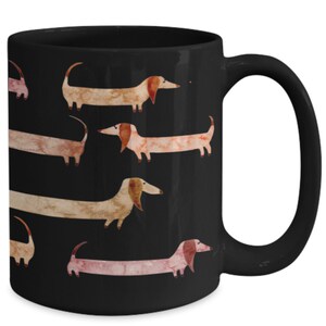 May include: Black ceramic mug featuring a repeating pattern of watercolor dachshunds in shades of brown, tan, and pink. The dogs have long bodies and floppy ears. The mug has a curved handle.