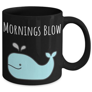 May include: Black coffee mug with a white whale graphic and the text "Mornings Blow" in white.
