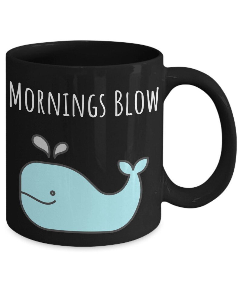 May include: Black coffee mug with a white whale graphic and the text "Mornings Blow" in white.