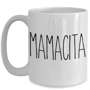 May include: White ceramic mug with the word "MAMACITA" printed in black, handwritten-style lettering. The mug has a curved handle and a glossy finish. A simple, everyday coffee mug.
