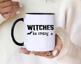 May include: White ceramic mug with a black handle and rim. The mug features the text "WITCHES be crazy" in black, along with a bat and spider graphic, perfect for Halloween or a witchy theme.