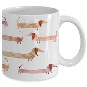May include: White ceramic coffee mug with a pattern of watercolor dachshunds in shades of brown, pink, and orange.