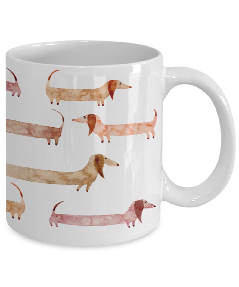 May include: White ceramic coffee mug with a pattern of watercolor dachshunds in shades of brown, pink, and orange.