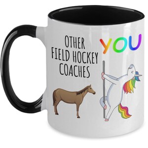 May include: White coffee mug with a black rim and handle. The mug has a graphic of a unicorn and a horse with the text "Other Field Hockey Coaches" and "You" on the mug.