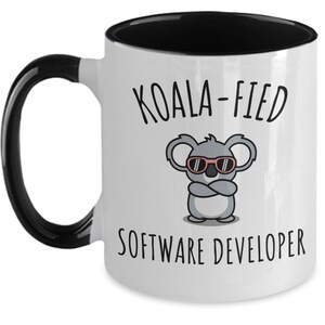 May include: White coffee mug with a black rim and handle. The mug has a black and white illustration of a koala wearing sunglasses and the text "Koala-fied Software Developer".