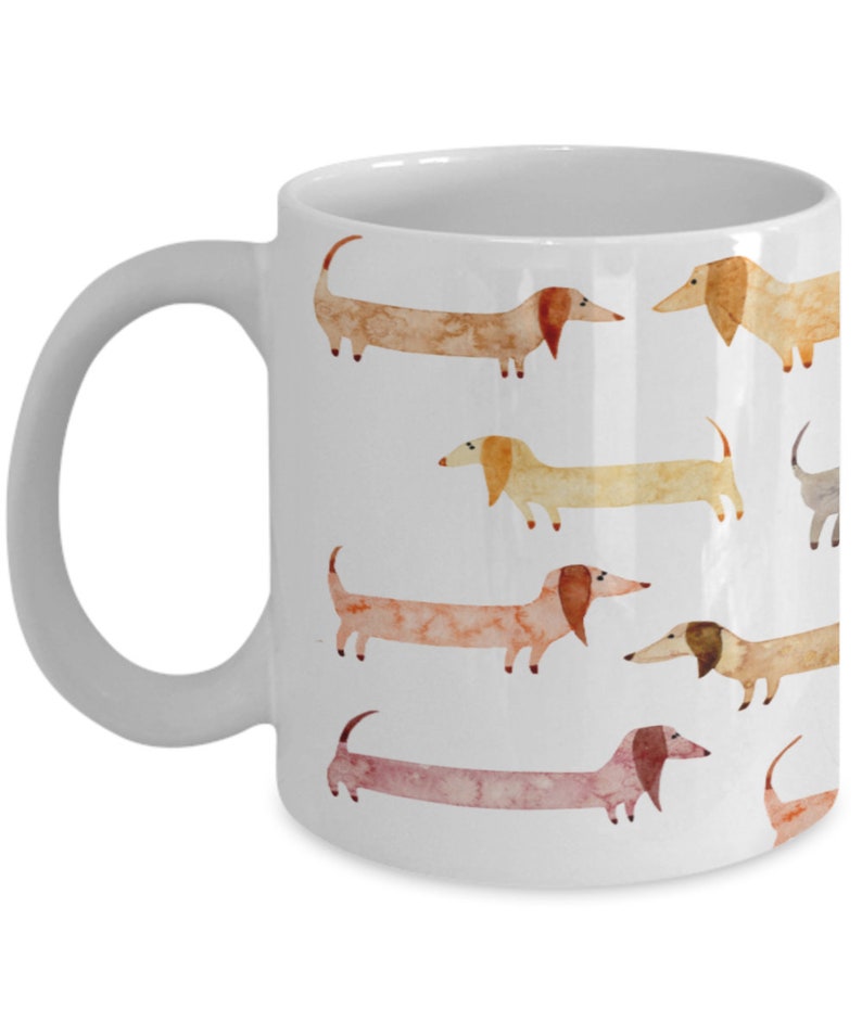 May include: White ceramic coffee mug with a pattern of watercolor dachshunds in various shades of brown, orange, and yellow.