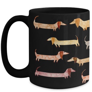 May include: Black ceramic mug featuring a repeating pattern of watercolor dachshunds in various colors. The dogs have long bodies, short legs, and floppy ears. The mug has a curved handle and a glossy finish.