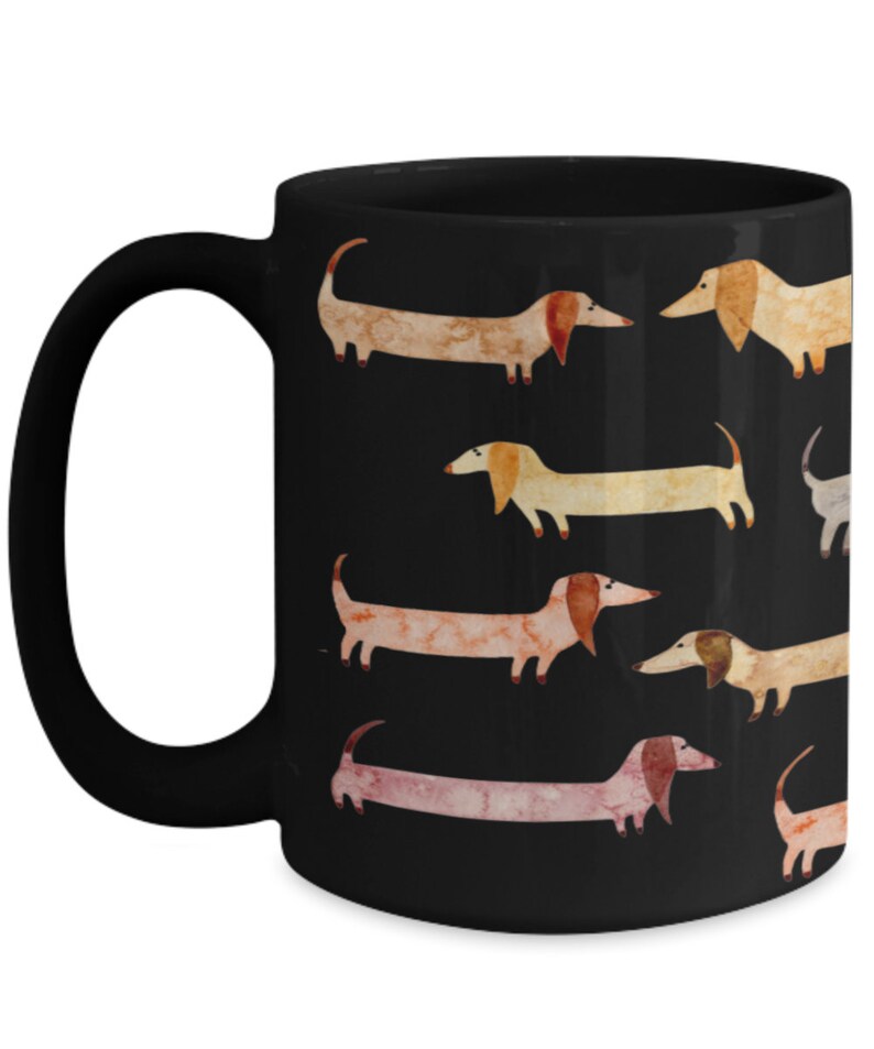 May include: Black ceramic mug featuring a repeating pattern of watercolor dachshunds in various colors. The dogs have long bodies, short legs, and floppy ears. The mug has a curved handle and a glossy finish.