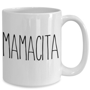 May include: White ceramic mug with the word "MAMACITA" printed in black, sans-serif font. The mug has a curved handle and a glossy finish. The mug is designed for hot or cold beverages.