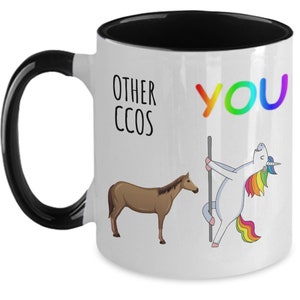 May include: White coffee mug with a black rim and handle. The mug has a graphic of a unicorn and a horse with the text "Other CCOS" and "YOU" in rainbow colors.