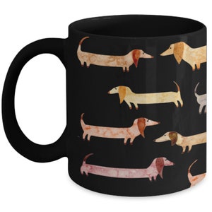 May include: Black ceramic mug featuring a repeating pattern of watercolor dachshunds in various shades of tan, pink, and cream against a black background. The mug has a black handle and a glossy finish, perfect for coffee or tea.