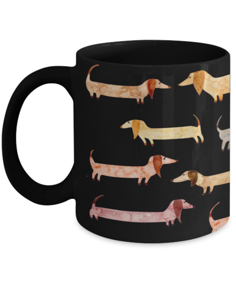 May include: Black ceramic mug featuring a repeating pattern of watercolor dachshunds in various shades of tan, pink, and cream against a black background. The mug has a black handle and a glossy finish, perfect for coffee or tea.
