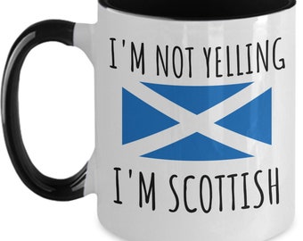 Pode incluir: Caneca de café de cerâmica branca com borda e alça pretas. A caneca tem um design de bandeira escocesa preta e azul e o texto "Não estou gritando, sou escocês".