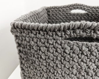 May include: A gray knitted storage basket with two handles. The basket is made of a thick, textured yarn.
