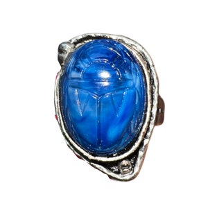May include: A silver ring with a blue scarab beetle design. The beetle is carved into the stone and has a detailed design.
