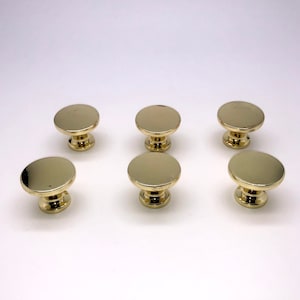 May include: Six gold-toned round cabinet knobs with a raised, circular design. The knobs have a smooth, polished finish.