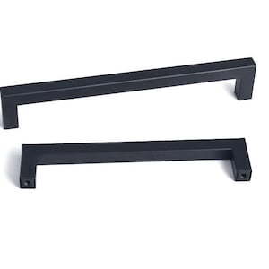May include: Two black metal cabinet pulls with a rectangular shape and a slight curve. The pulls have a matte finish.