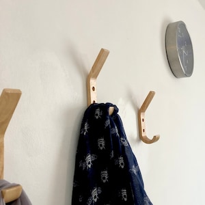 May include: Three wooden wall hooks with a scarf hanging on one of them. The scarf is blue with a white bee pattern.