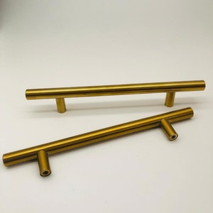May include: Two gold-toned metal cabinet pulls with a simple, straight design. The pulls are approximately 10 inches long.