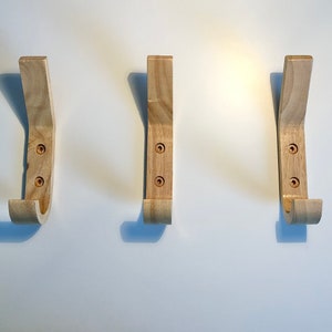 May include: Three wooden wall hooks with a curved design. The hooks are light brown and have two visible screws each.