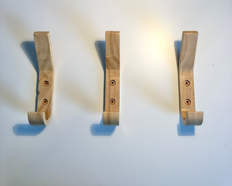 May include: Three wooden wall hooks with a curved design. The hooks are light brown and have two visible screws each.