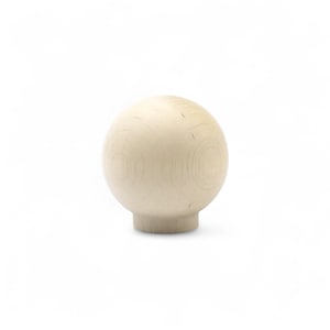 Può includere: Un pomello sferico in legno di colore chiaro con una base cilindrica corta. La venatura del legno è visibile sulla superficie della sfera. Il pomello è probabilmente per mobili o scopi decorativi.