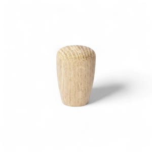 Puede incluir: Un tapón de mueble de madera de color claro con una parte superior redondeada y un cuerpo cónico. El tapón está hecho de madera sin terminar, mostrando la veta y la textura naturales. El tapón está diseñado para encajar en un agujero pretaladrado.