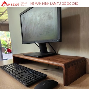 May include: A dark brown wooden monitor stand with a curved design. The stand is made of solid wood and features a keyboard and mouse in front of a black computer monitor. The stand is approximately 24 inches wide.