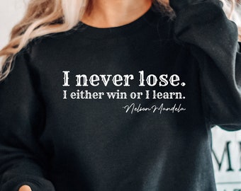 May include: A black sweatshirt with the quote "I never lose. I either win or I learn." by Nelson Mandela printed in white on the front.