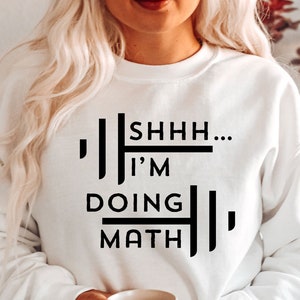 May include: White sweatshirt with black text that reads "Shhh... I'm doing math". The sweatshirt is being worn by a person holding a white mug.