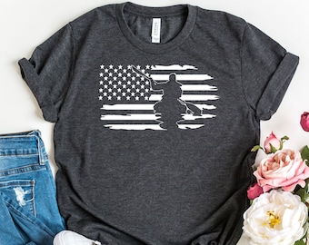 Könnte beinhalten: Ein dunkelgraues T-Shirt mit einem weißen, abgenutzten amerikanischen Flaggen-Design, das die Silhouette einer Person im Kajak zeigt.