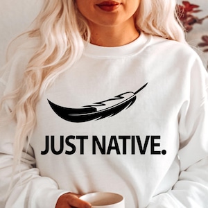 May include: White sweatshirt with a black feather design and the text "JUST NATIVE."
