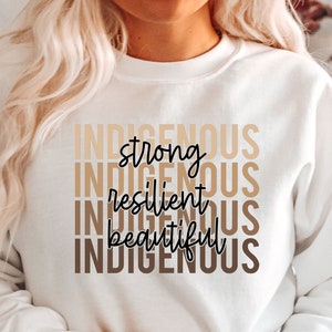 Może przedstawiać: Biała bluza z nadrukiem "INDIGENOUS strong INDIGENOUS resilient INDIGENOUS beautiful INDIGENOUS" w brązowych i czarnych literach.