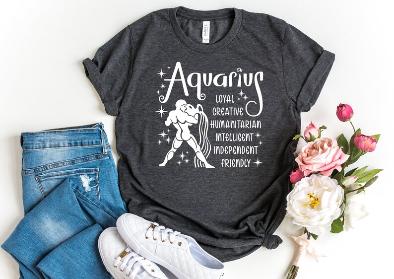 May include: A dark heather gray short-sleeve t-shirt featuring a white graphic of the Aquarius zodiac sign. The design includes the word Aquarius, a figure pouring water, and the words loyal, creative, humanitarian, intelligent, independent, friendly.