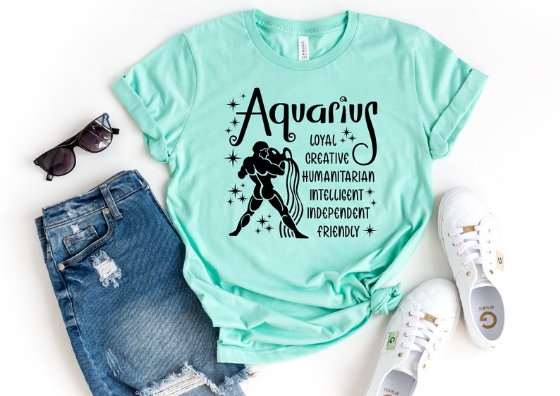 May include: A mint green t-shirt featuring a black graphic of the Aquarius zodiac sign, a figure pouring water, and the words Aquarius, Loyal, Creative, Humanitarian, Intelligent, Independent, and Friendly, surrounded by small star icons.