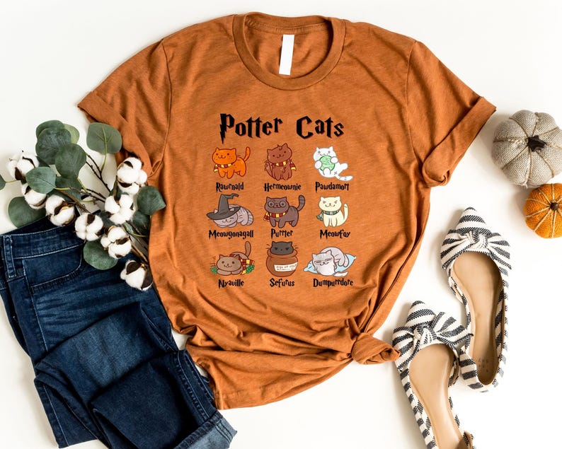 May include: A brown t-shirt with the text "Potter Cats" and illustrations of cats with names like "Ronweald", "Hermione", "Padma", "Neville", "Sirius", and "Dumbledore".