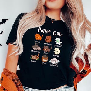 May include: Black t-shirt with a graphic of cats representing characters from the Harry Potter series. The text "Potter Cats" is printed above the graphic.