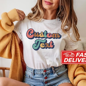 May include: White t-shirt with the words "Custom Text" in a retro font, featuring shades of pink, orange, teal, and blue. A red "Fast Delivery" sticker is visible. The shirt is part of a clothing collection.
