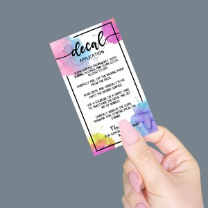 May include: A colorful card with watercolor splatter designs and instructions for applying a decal. The text reads "decal application" and includes steps for cleaning the surface, peeling the decal, and smoothing it out.
