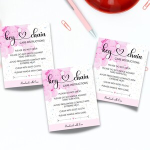 May include: Three pink and white key chain care instruction tags with a pink watercolor background and white glitter. The text on the tags reads "key chain" and "Care Instructions". The instructions include "Please do not drop", "Please do not knock against hard surfaces", "Avoid prolonged contact with extreme heat", "Clean with soft cloth", and "Please handle with care". The bottom of each tag reads "Handmade with Love".
