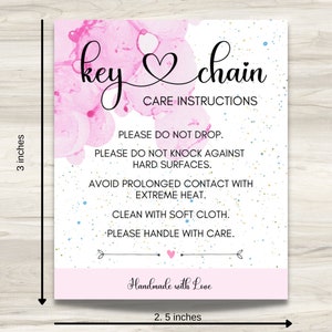 May include: Pink and white care instructions card for a key chain. The card has a pink watercolor background with gold and blue glitter. The text reads "key chain" with a heart symbol and "Care Instructions". The instructions are: "Please do not drop. Please do not knock against hard surfaces. Avoid prolonged contact with extreme heat. Clean with soft cloth. Please handle with care." The card also says "Handmade with Love".