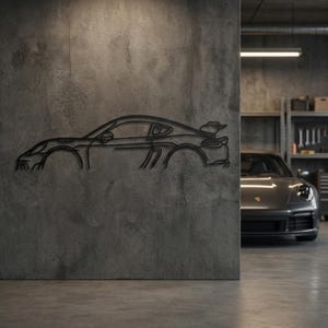 May include: A dark gray metal wall art piece depicting the side profile of a sports car. The artwork is mounted on a textured concrete wall. A gray sports car is parked in the background, visible through an opening.
