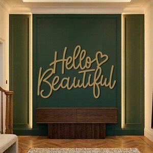 Può includere: Un'opera d'arte da parete in legno con la scritta "Hello Beautiful" in corsivo, montata su una parete verde scuro. Sotto c'è un mobile in legno con una base a coste. La stanza ha un design moderno.