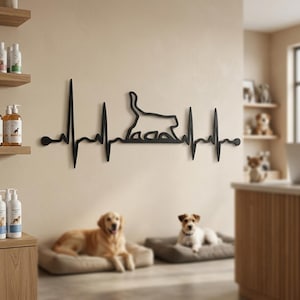Puede incluir: Arte mural de metal negro que representa la silueta de un gato dentro de un diseño de latido cardíaco. La obra de arte está montada en una pared beige. Dos perros descansan en camas para perros debajo.