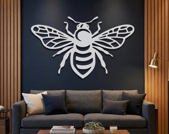 May include: A large, white metal bee wall art decor. The bee is mounted on a dark blue wall above a gray sofa with throw pillows. The bee has detailed wings and body segments, adding a modern touch to the living room.