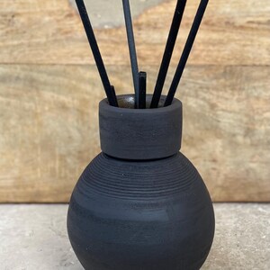 May include: Black ceramic diffuser bottle with a round, textured body and a black lid.  Black diffuser sticks are inserted into the bottle.
